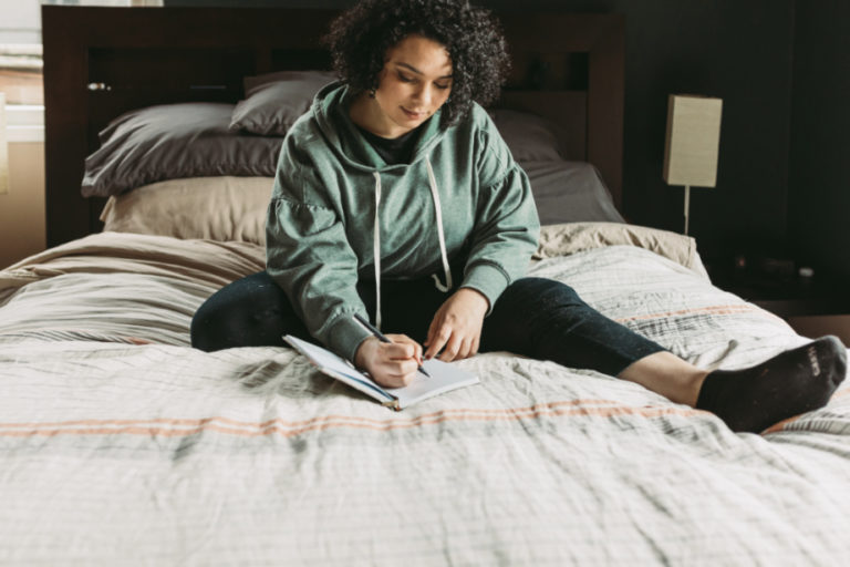 Woman sitting on her bed and writing in a notebook.
