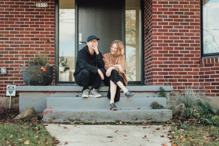 Man and woman sitting on stoop and laughing with fall leaves on the ground.