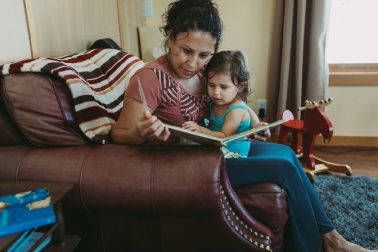 Woman reading storybook to toddler girl.