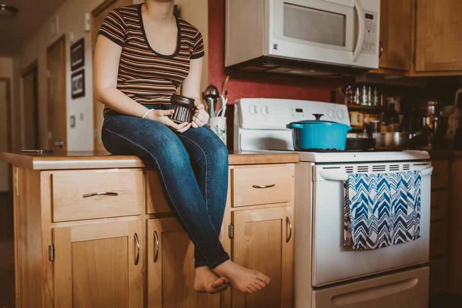 Woman sitting on kitchen counter with cup of coffee or tea.