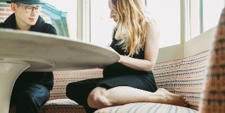Pregnant woman sits at table and reads.