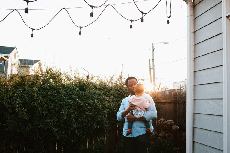 Man holds a baby in a backyard at sunset.