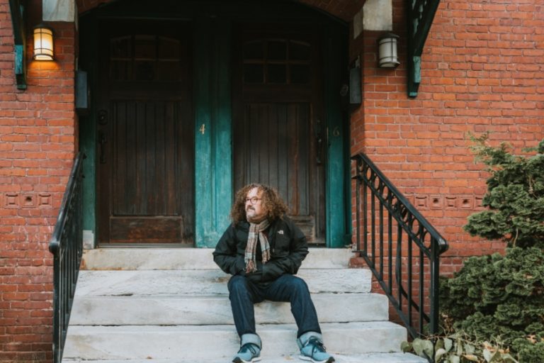 Man sitting on stoop in front of brick townhome.