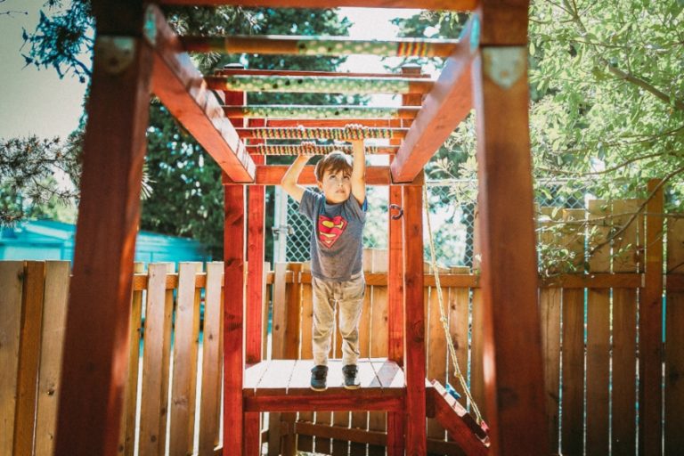 Child wearing a Superman shirt playing on a swing set.
