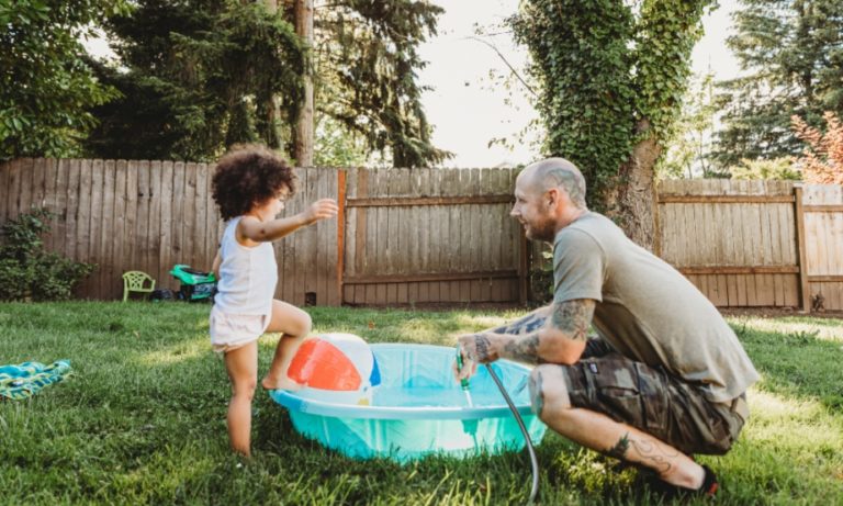 Dad playing with toddler girl in backyard kiddie pool.