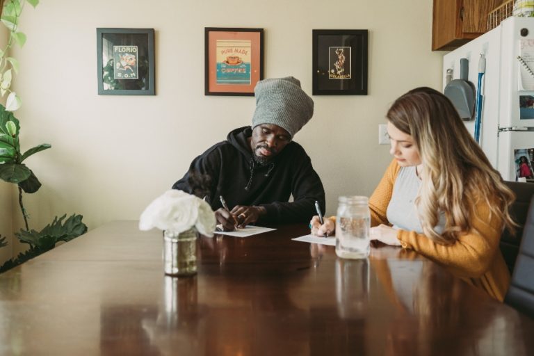 Man and woman sit at dining room table filling out paperwork.