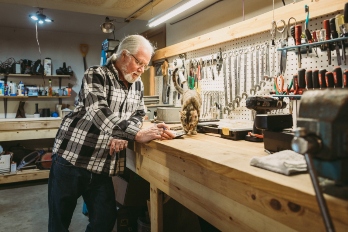 Man stands with his cat at a workbench in his garage.