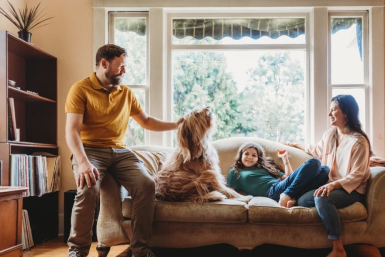 Family hangs out on their living room sofa with their big fluffy dog.