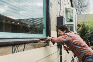 Man repairs area around exterior of window outside his home.