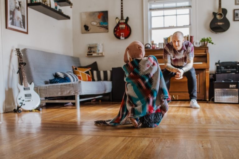 Little girl walks toward her dad wrapped in a blanket in a living room filled with musical instruments.