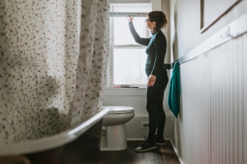 Woman hangs a shade in a bathroom window.